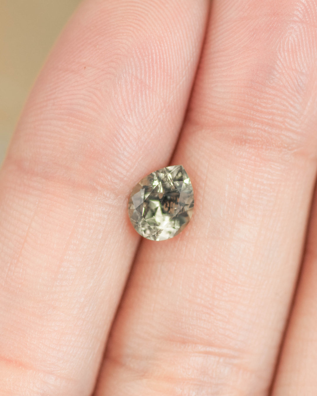 Light teal pear-shaped Montana sapphire displayed on fingertip for scale, showing true size, natural color, and precision cut sapphire proportions.