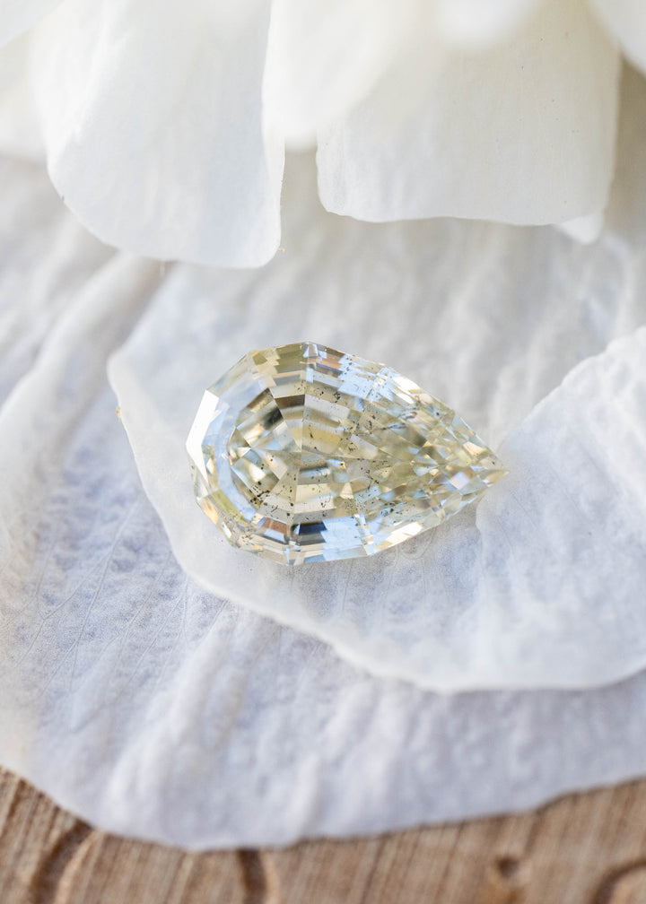 Light Yellow Geo Pear step cut diamond resting on white flower petals, displaying warm golden tones, crisp geometric faceting, and natural inclusions.