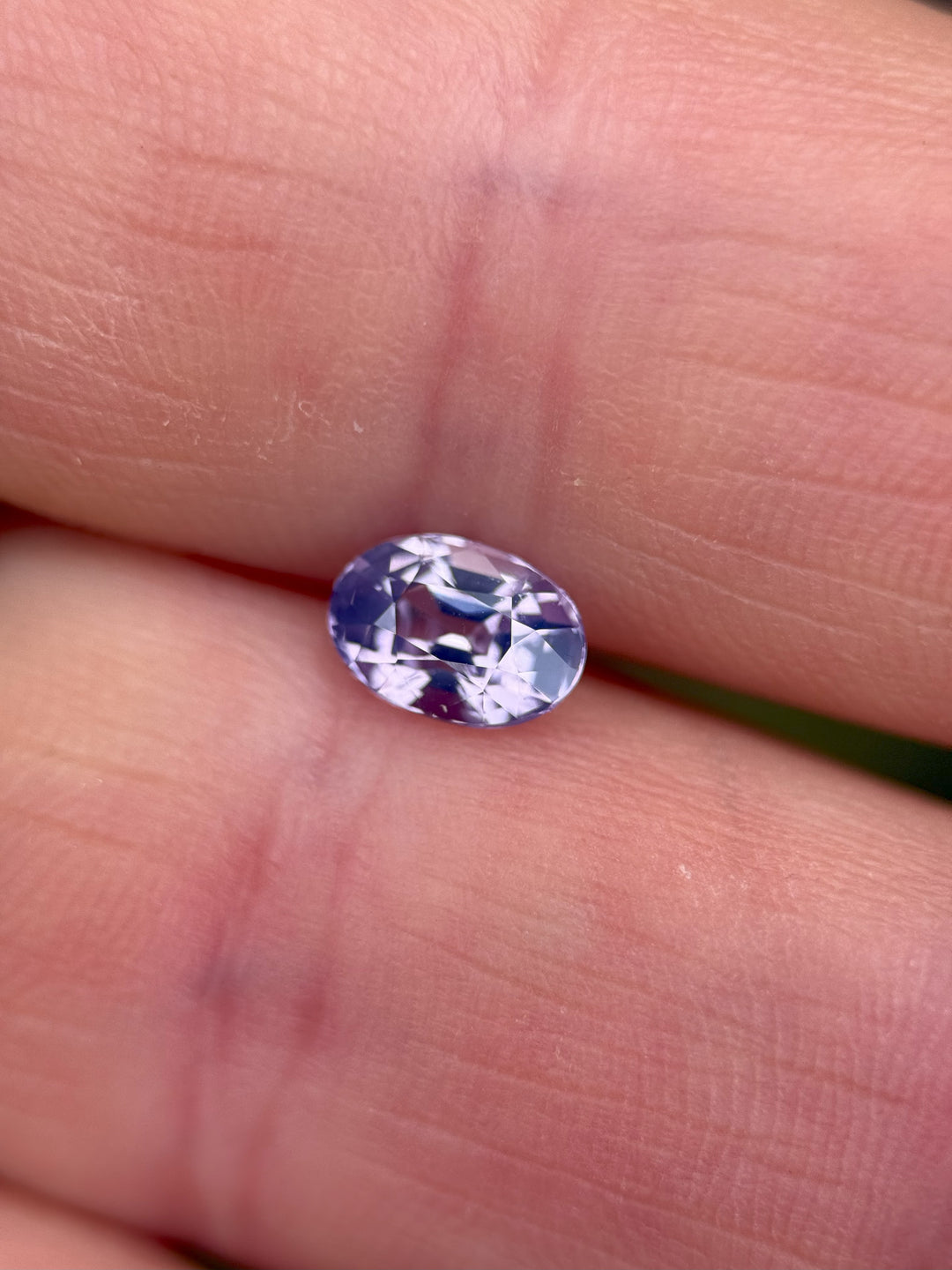 1.18ct bi-color oval sapphire held between fingertips, glowing with lilac and lavender hues