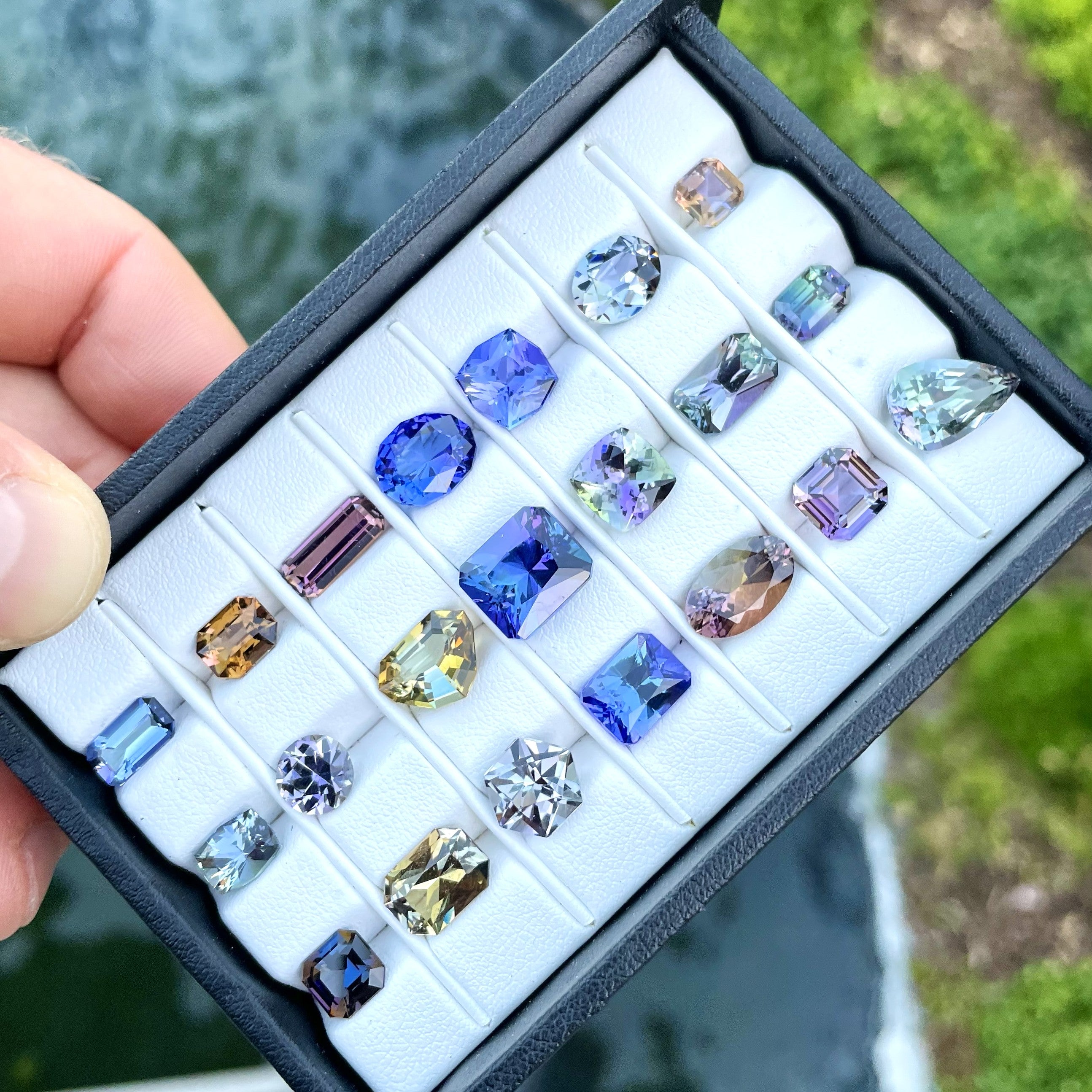 Hand holding a tray of colorful loose gemstones in mixed cuts and colors, selected for custom jewelry, client projects, and designer sourcing.