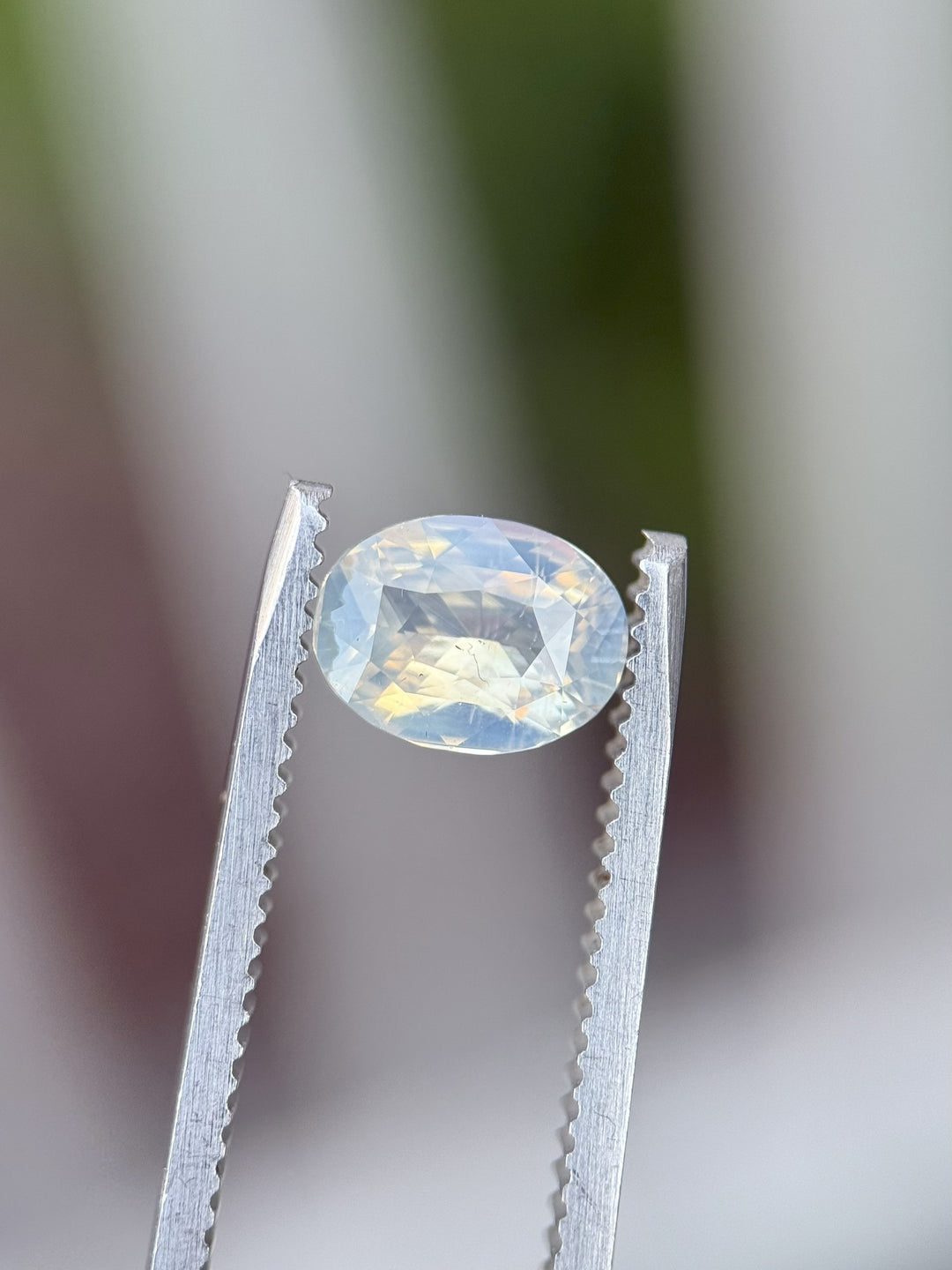 1.50 carat untreated sapphire from Madagascar held in tweezers showing soft opalescent and peach hues in a custom brilliant oval cut
