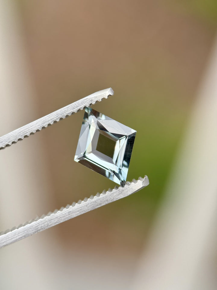 Close-up of 2.68ct sapphire in precision lozenge kite cut held in tweezers, shifting from greenish blue to steely purple tones