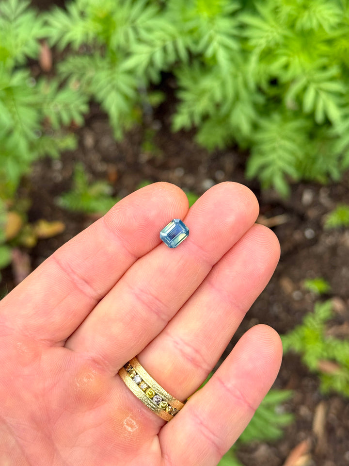 Madagascar sapphire resting on fingertips, showing a unique blend of yellow-green and blue-teal hues with soft internal glow.