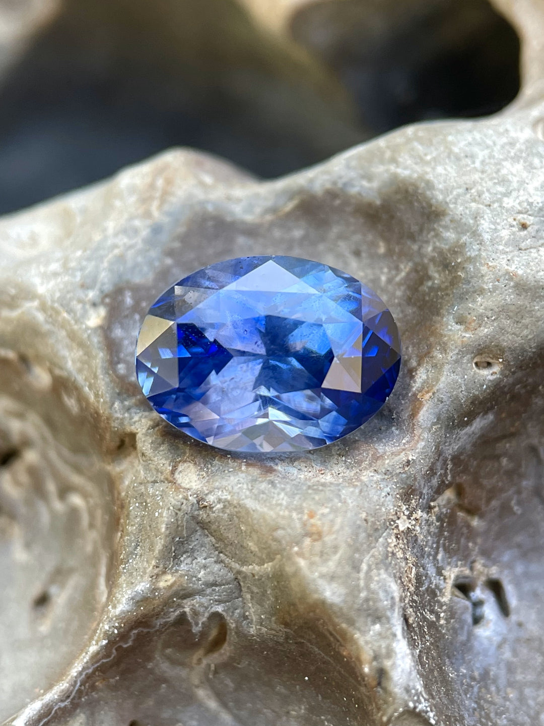 A close-up view of a 4.51ct Sri Lanka cornflower blue sapphire resting on a textured stone surface, emphasizing its mesmerizing color and faceting.