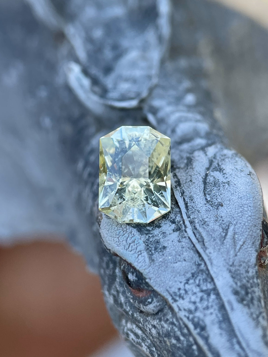 Close-up of a 2.04-carat yellow-green sapphire resting on textured sculpture, showcasing its unique custom elongated octagon brilliant cut.
