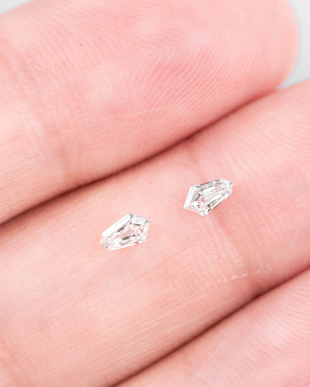Matched pair of 0.23 carat F–G color VVS clarity kite step cut diamonds displayed on fingers, showcasing the precision geometric faceting and brilliance of the loose South African stones.