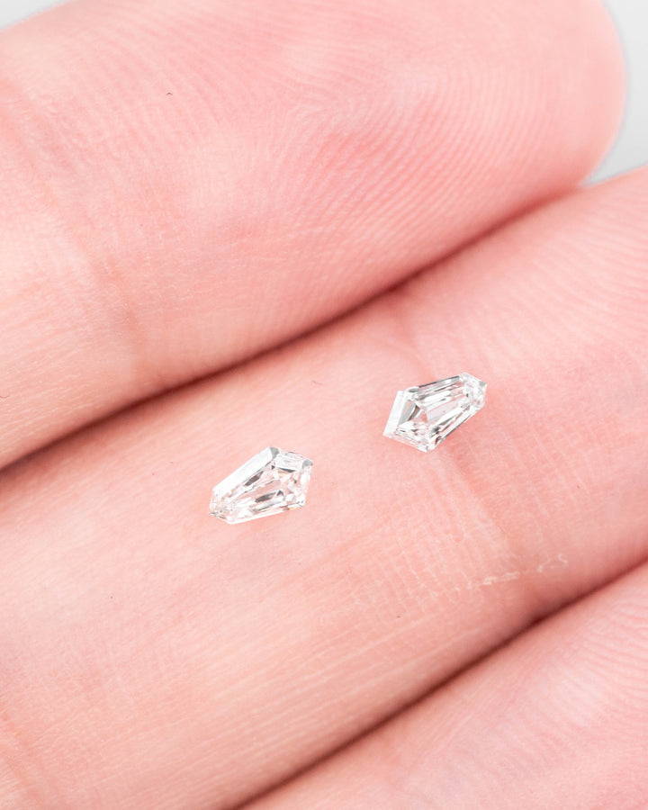 Matched pair of 0.23 carat F–G color VVS clarity kite step cut diamonds displayed on fingers, showcasing the precision geometric faceting and brilliance of the loose South African stones.