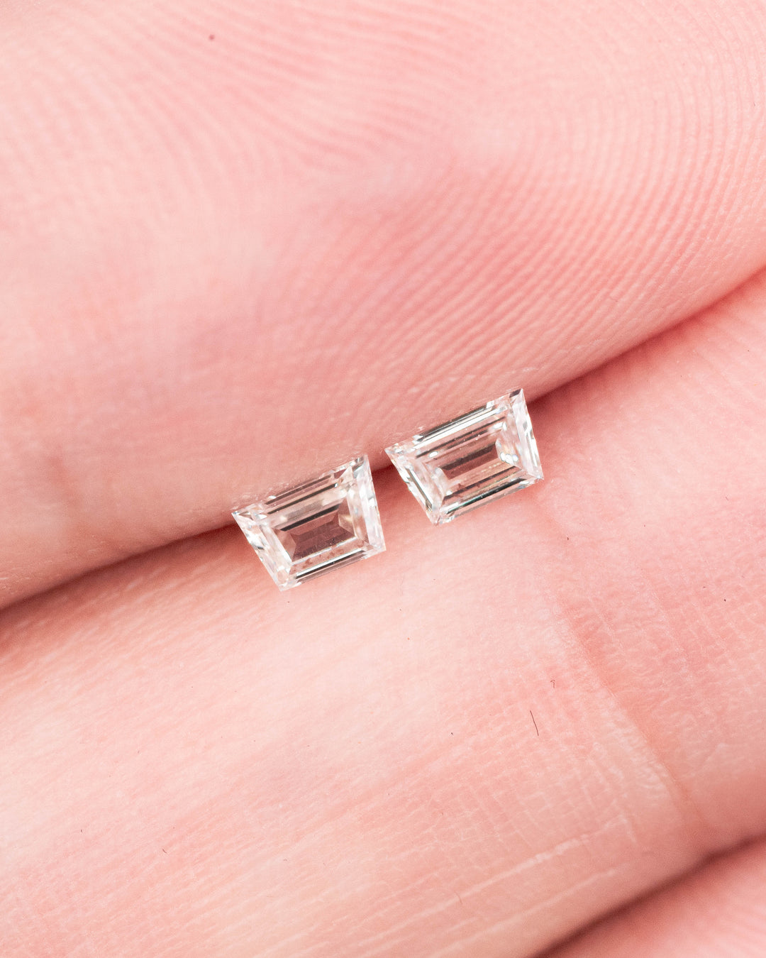 0.28 carat F–G color VVS clarity Trapezoid step cut diamond pair displayed on fingertips, showing the precise step-cut facets, matched proportions, and clarity of two untreated South African diamonds for jewelry design.