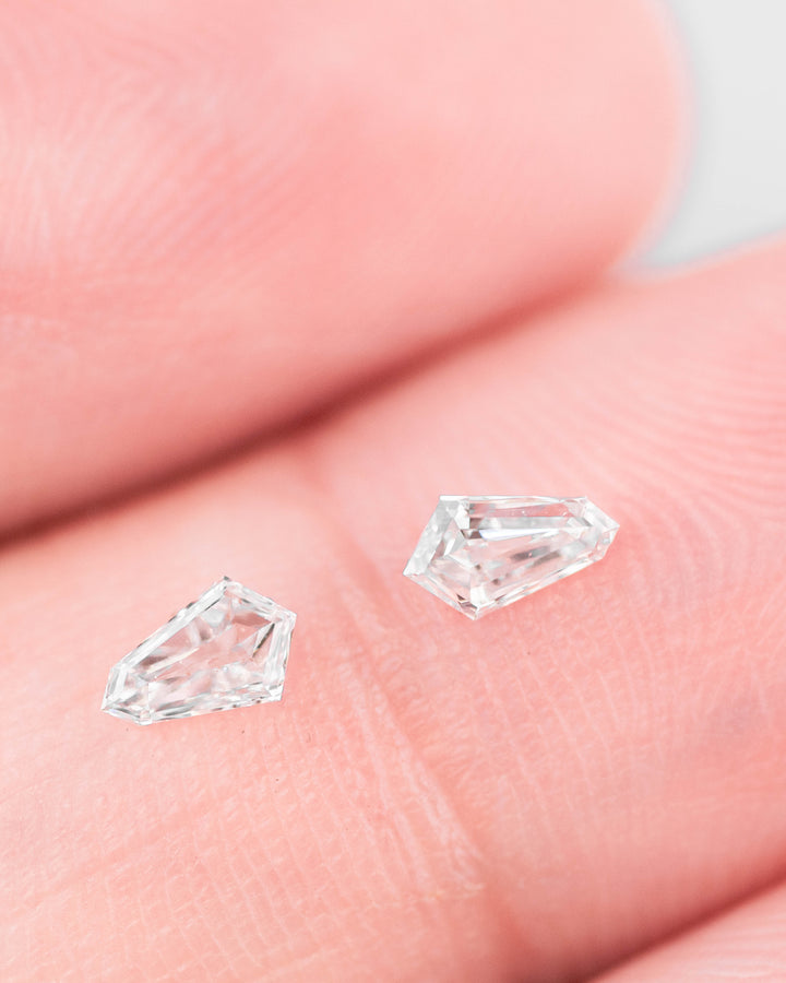 0.28 carat G color VVS clarity kite step cut diamond pair resting on a fingertip, showing size reference, faceting detail, and sparkle of the precision-cut South African diamonds.