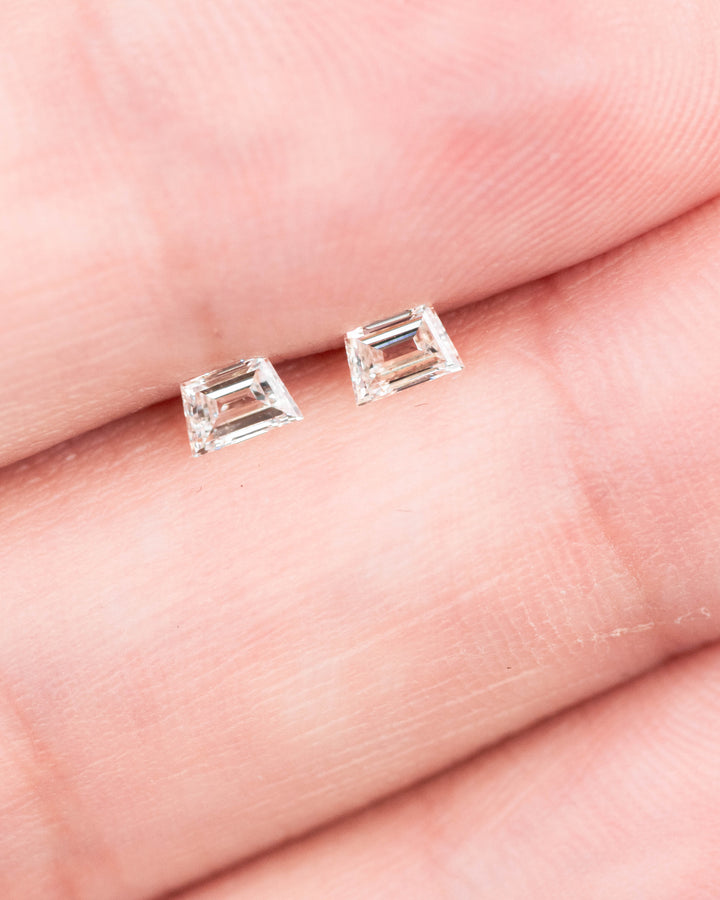 0.29 carat matched pair of G–H color VVS clarity trapezoid step cut diamonds displayed on fingertips, showing the clean step faceting, symmetry, and brilliance of untreated South African diamonds.
