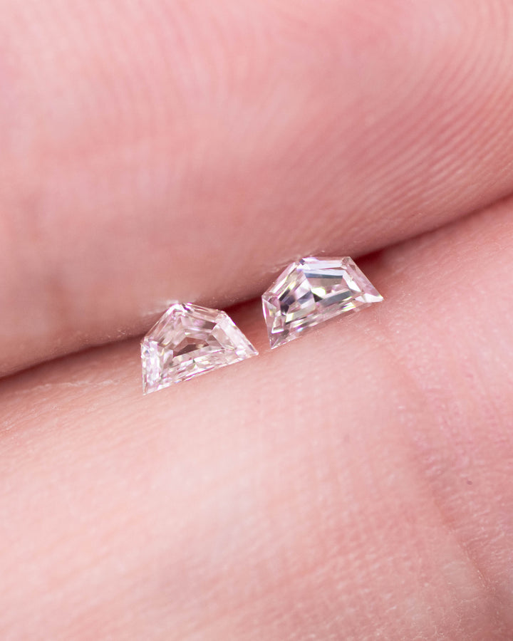 Close-up of a 0.18 carat D–E color VVS clarity Cadillac cut diamond pair from South Africa displayed on a fingertip. The natural untreated diamonds show perfect geometric faceting and exceptional sparkle.
