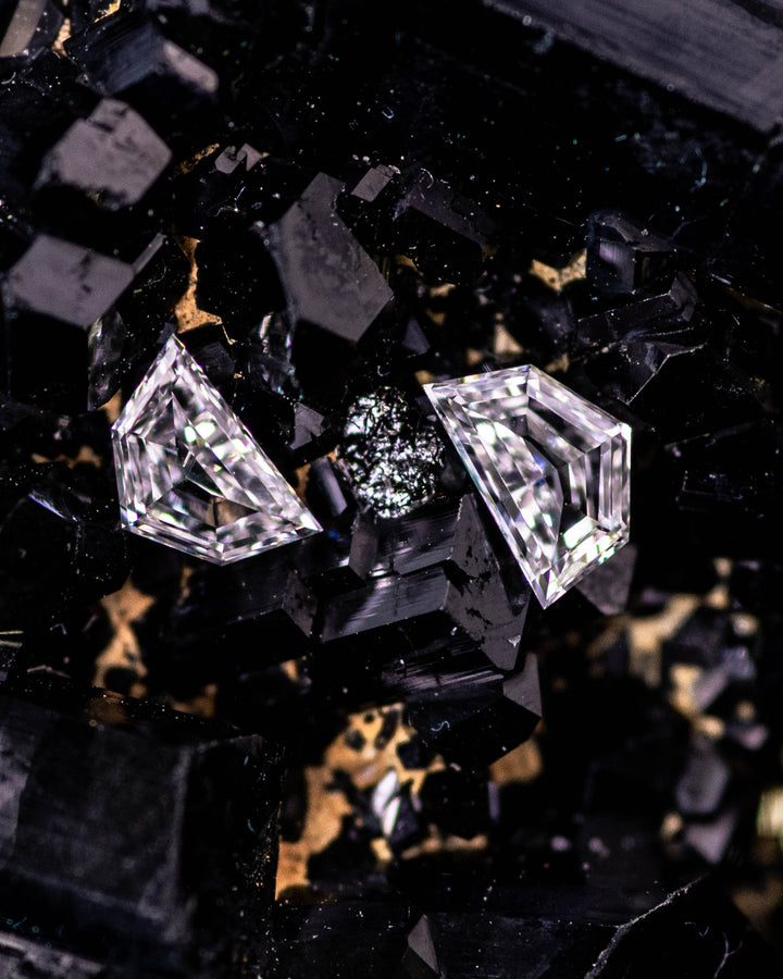 Macro photo of a matching pair of 0.18 carat E–F color VVS clarity Cadillac cut diamonds from South Africa resting on dark tourmaline crystal. The natural untreated stones display perfect symmetry and geometric precision