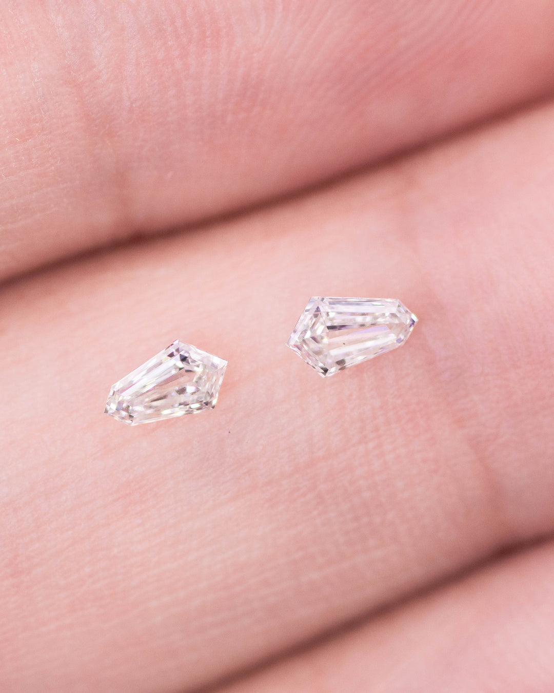 Macro photo of a 0.28 carat G–H color VVS clarity Cadillac cut diamond pair from South Africa displayed on a fingertip. The natural untreated diamonds exhibit crisp symmetry, elegant faceting, and superior light reflection.