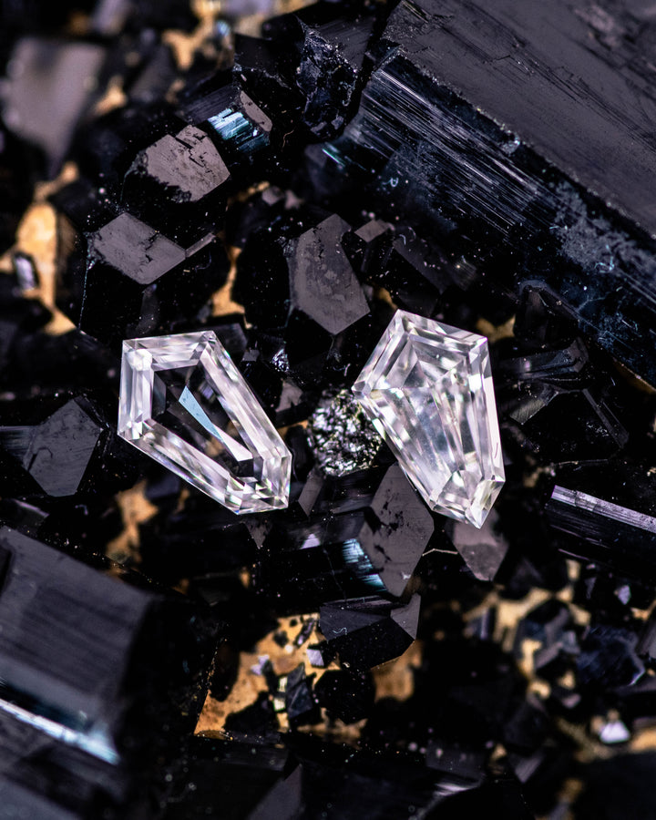 Macro photograph of two 0.29 carat F–G color VVS–VS clarity Cadillac cut diamonds from South Africa placed on dark mineral crystals. The ethically sourced stones highlight geometric precision and natural brilliance.