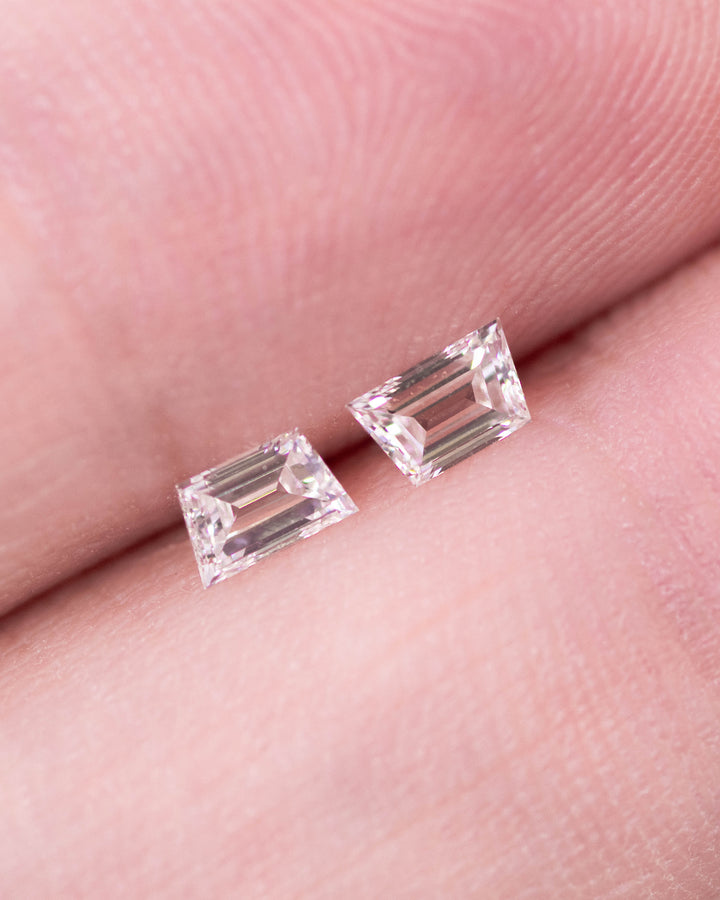 Close-up of 0.30 carat G color VVS clarity trapezoid step cut diamond pair from South Africa held on fingertips. The natural untreated diamonds showcase clean lines, crisp faceting, and perfect matching symmetry.