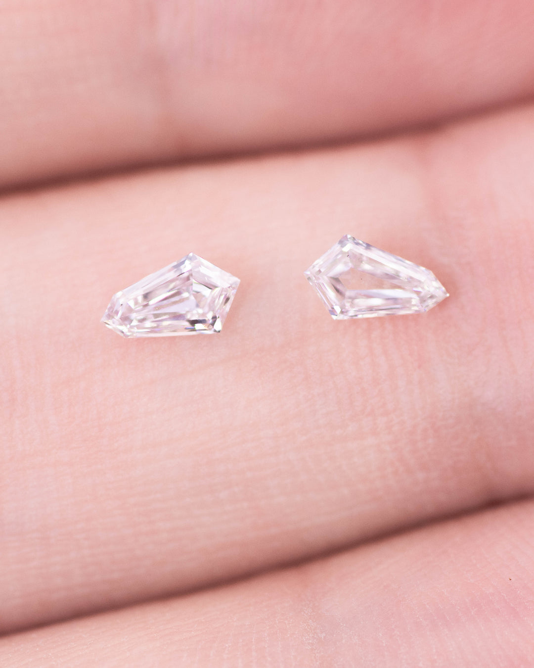 Close-up of a 0.34 carat D color VVS clarity kite step cut diamond pair from South Africa displayed on fingertips. The natural untreated diamonds show geometric precision, sharp facets, and elegant step-cut brilliance.