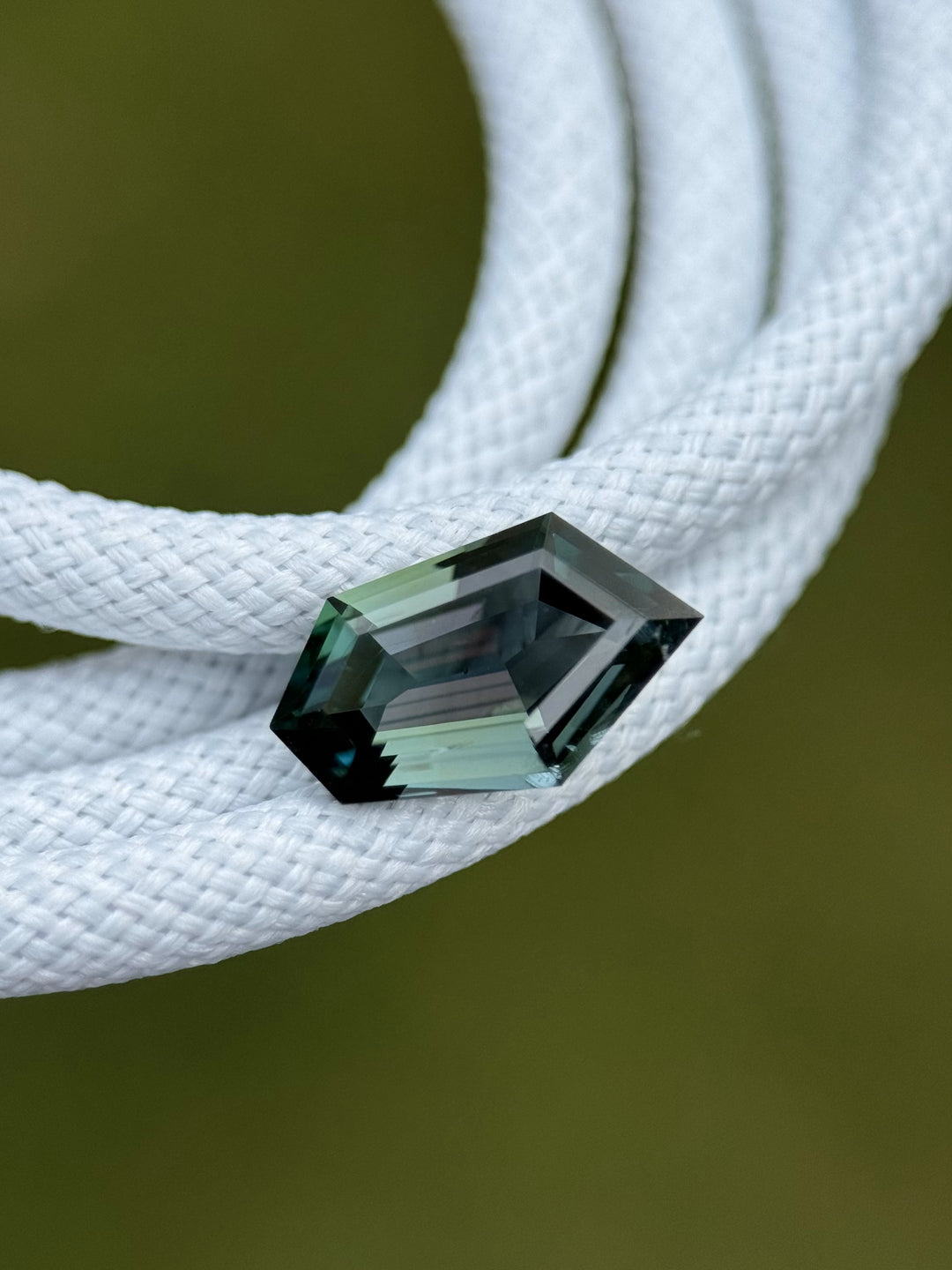 Freeform green tanzanite resting on coiled white cord, highlighting the brilliance and dimensional cut of the 1.55 carat gemstone