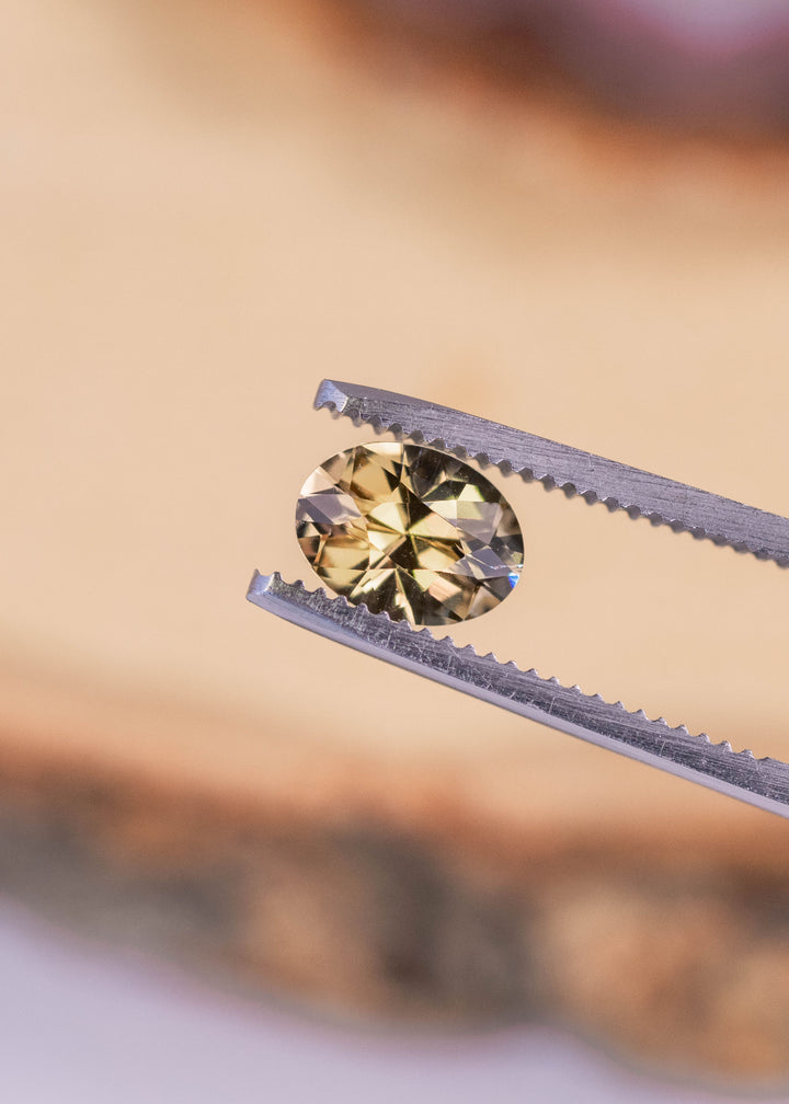 Custom mixed cut oval Tanzanite held in gem tweezers, displaying green and yellow hues with sharp facet reflections from Merelani Hills
