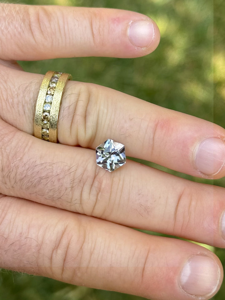 3.32-carat Tanzanite with custom hex cut shown on hand for scale, featuring vivid blue, green, and purple flashes.