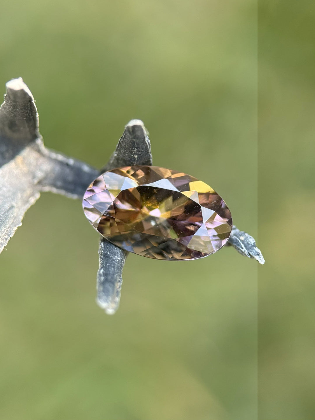 Macro view of reddish orange Tanzanite in claw tweezers, revealing precision facets and vivid internal fire