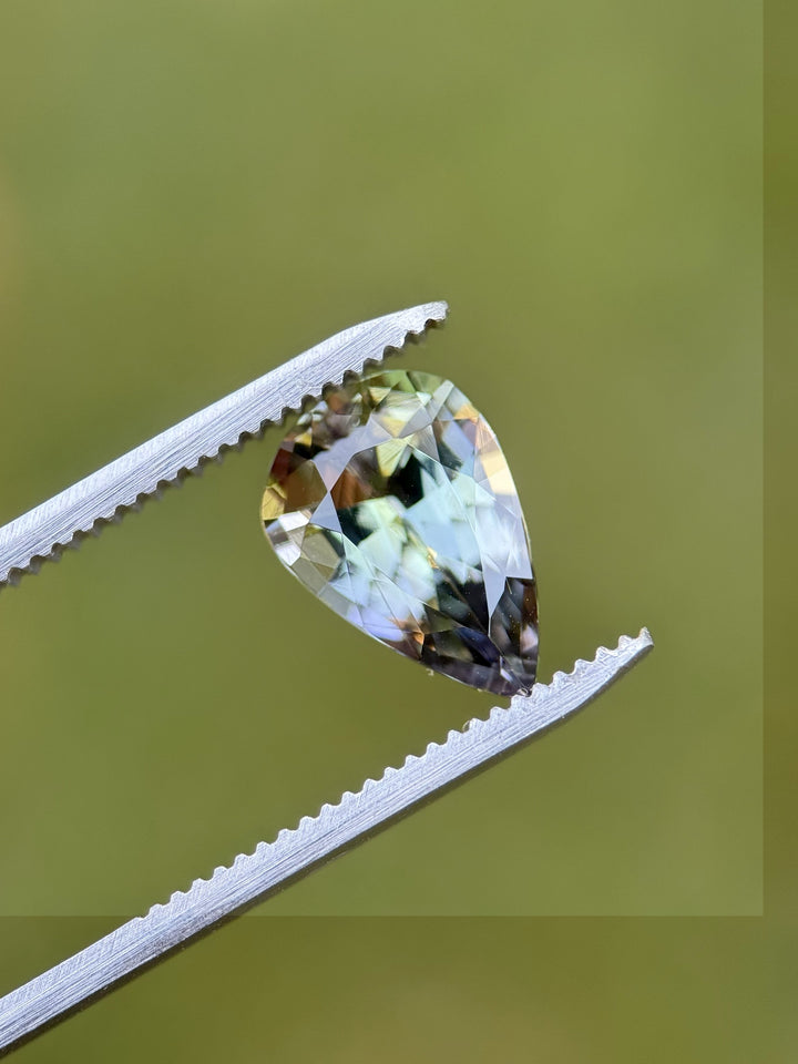 Pear-shaped Tanzanite held by tweezers against a green background