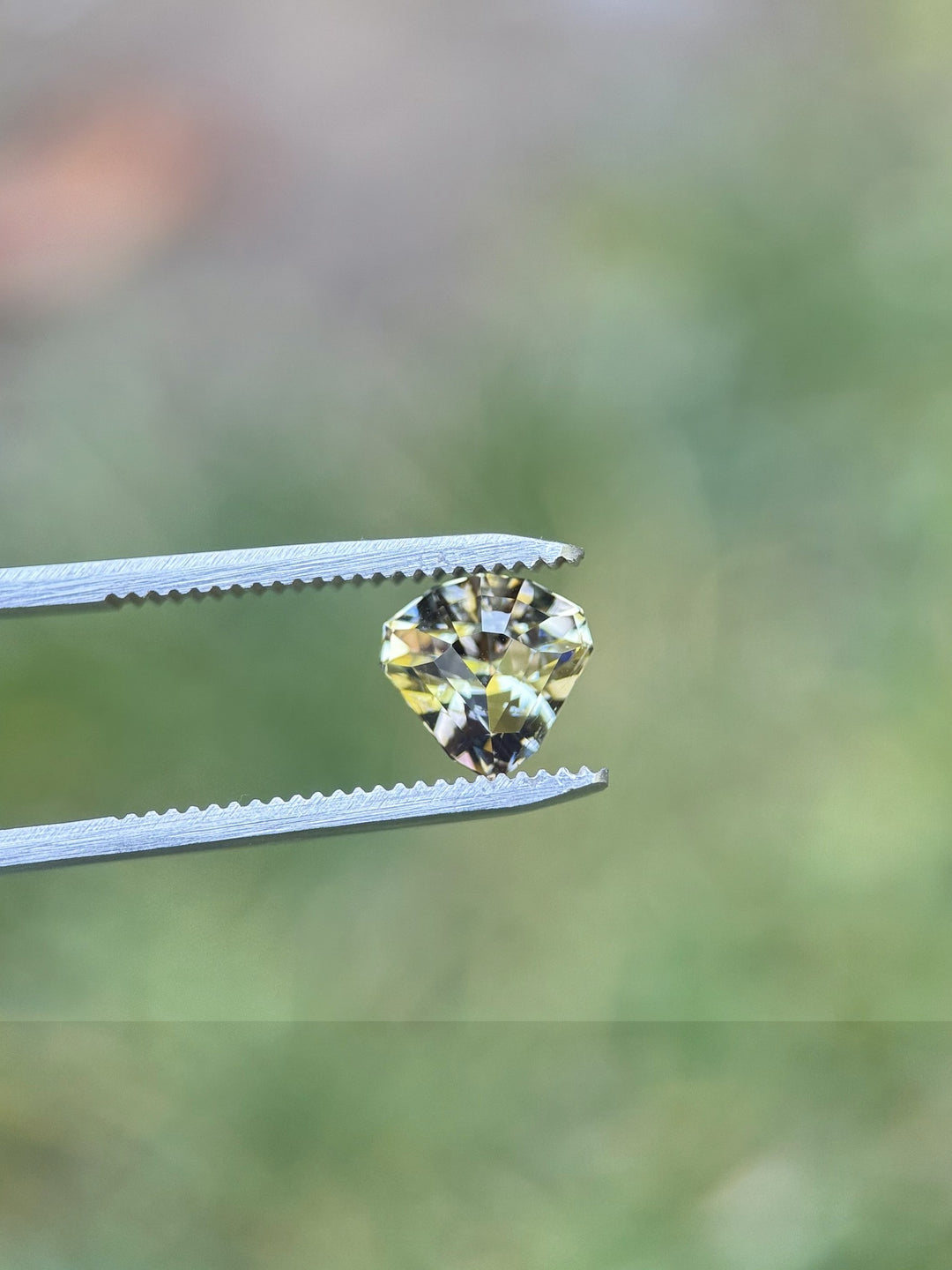 Fancy colored Tanzanite in tweezers – 2.87ct untreated shield-cut gem with peach, pink, and mermaid sparkle