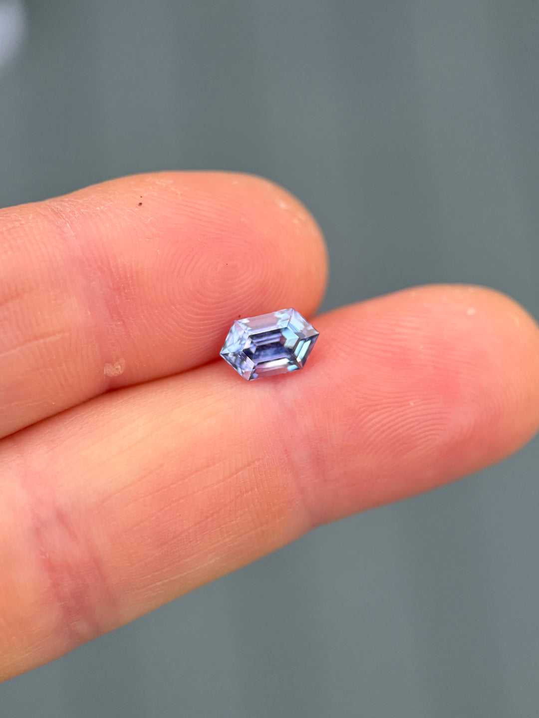 Mermaid-colored tanzanite weighing 1.43 carats in a precision step cut hexagon placed on fingertips, demonstrating its size, untreated clarity, and shifting blue, green, pink, and purple hues from Merelani Hills, Tanzania.