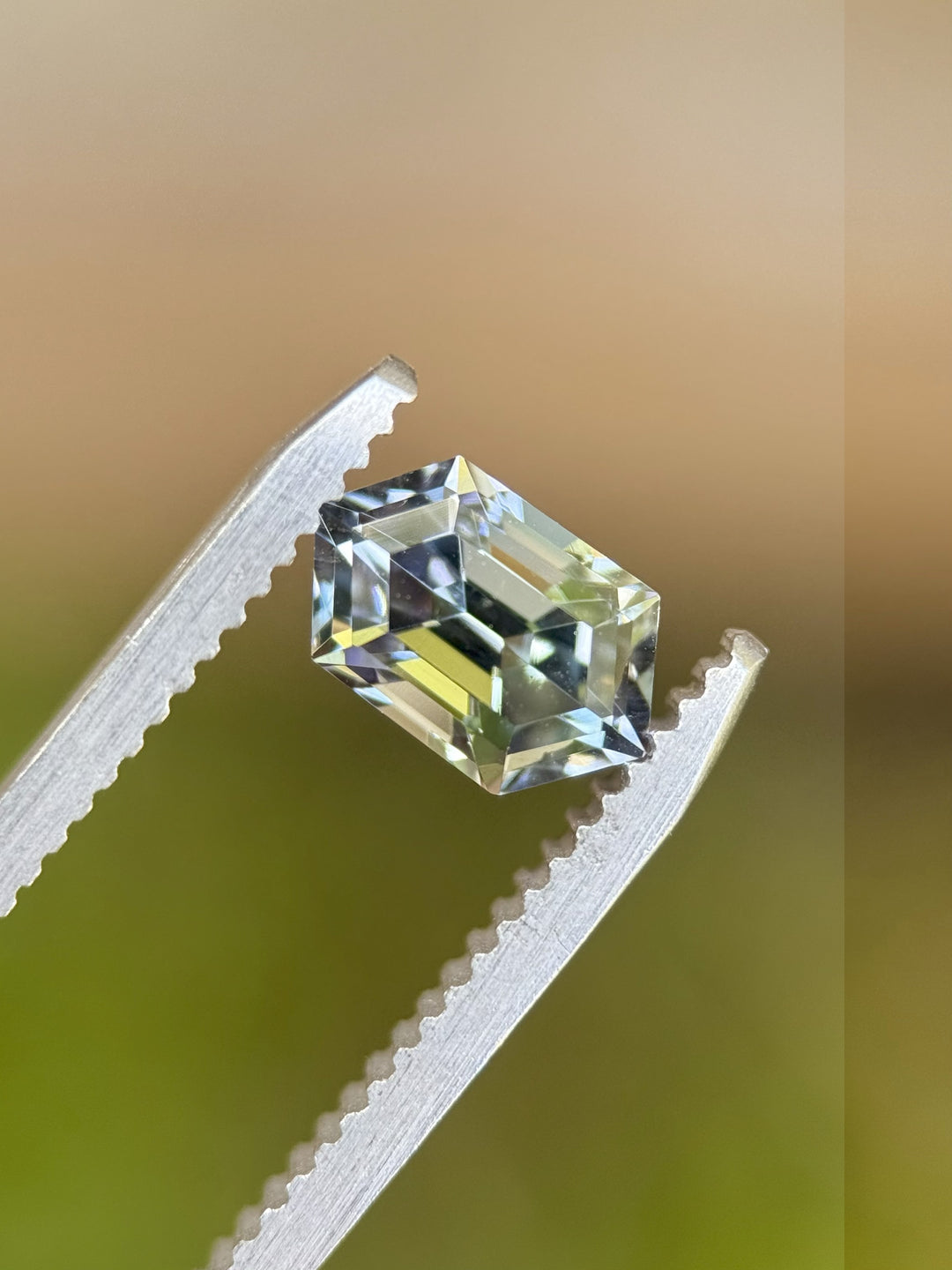 Close-up of teal blue-green Tanzanite in precision elongated hexagon step cut held by tweezers – 1.52 carats, unheated