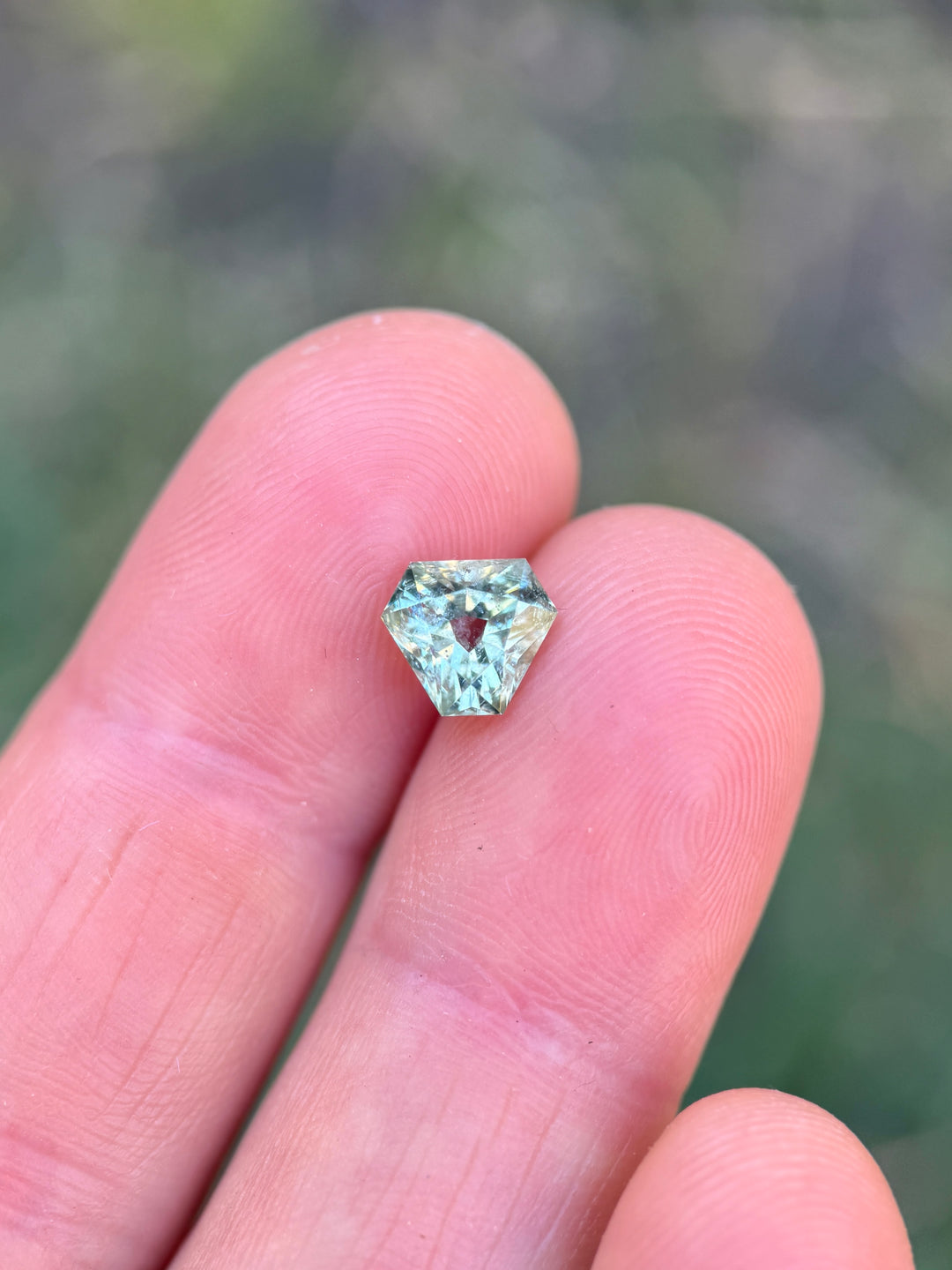 1.90 carat mint teal green sapphire resting on fingertips, showcasing custom antique cut corner trillion mixed cut and natural Montana sapphire color and brilliance