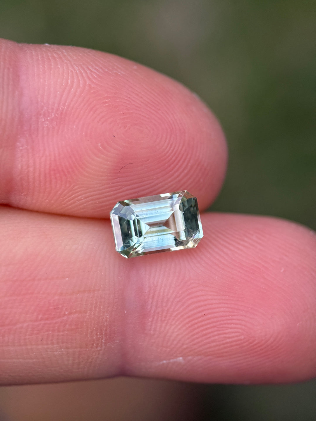 Mint green Madagascar sapphire resting on fingertips, showing lively color and transparent crystal structure.