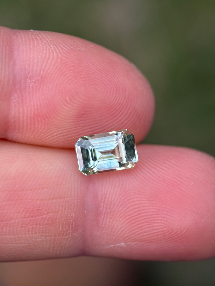 Mint green Madagascar sapphire resting on fingertips, showing lively color and transparent crystal structure.