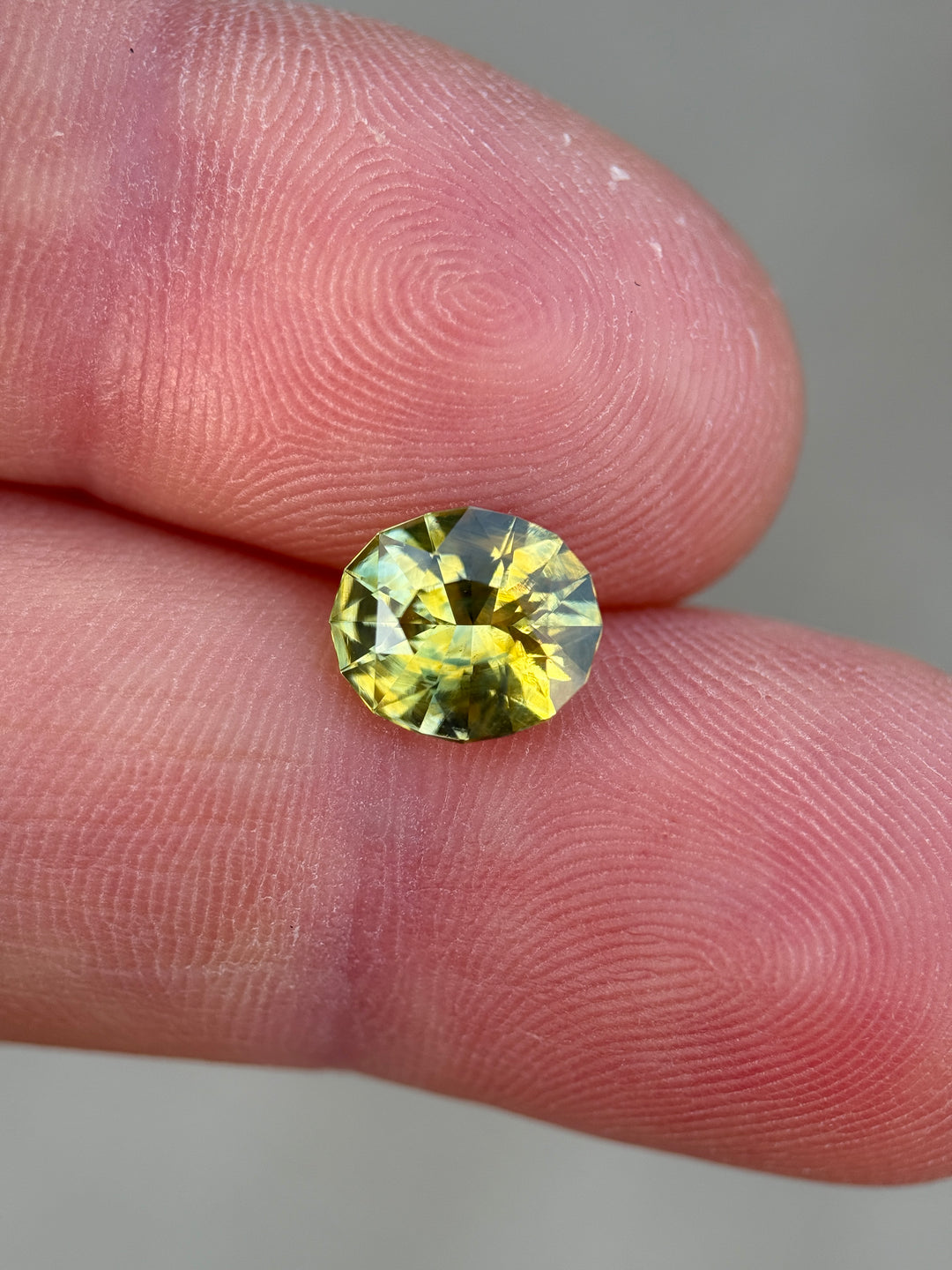 Modified oval mix cut Madagascar sapphire resting on fingertips, showing natural yellow-green color transitions and bright reflections.