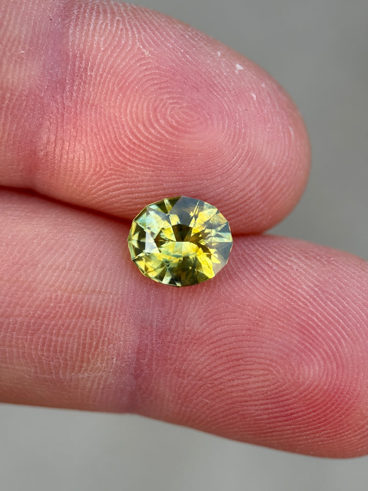 Modified oval mix cut Madagascar sapphire resting on fingertips, showing natural yellow-green color transitions and bright reflections.