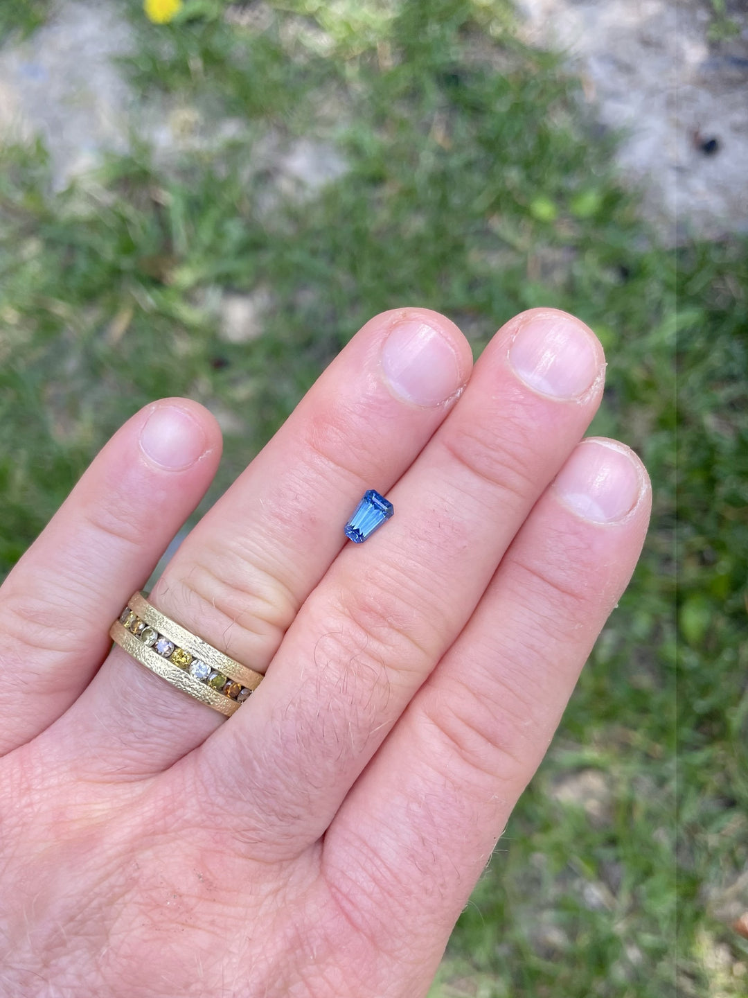 1.20 carat heated blue sapphire from Montana displayed on hand, showcasing precision tapered shield step cut and vibrant blue color.