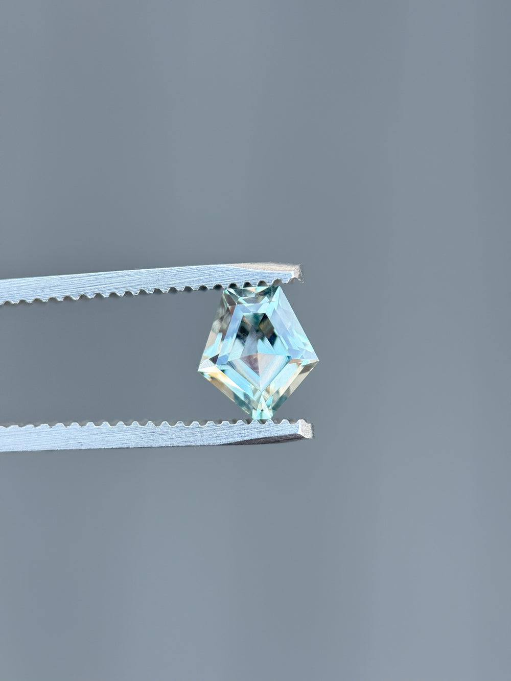1.50 carat Montana sapphire in shield step cut held by tweezers showing teal-blue brilliance