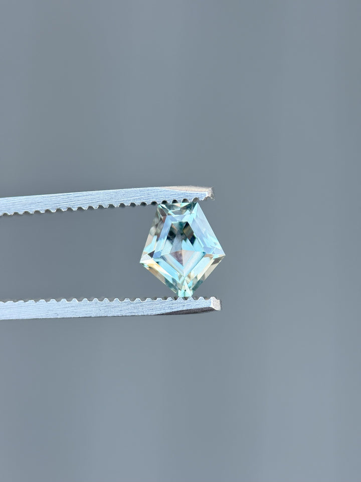 1.50 carat Montana sapphire in shield step cut held by tweezers showing teal-blue brilliance