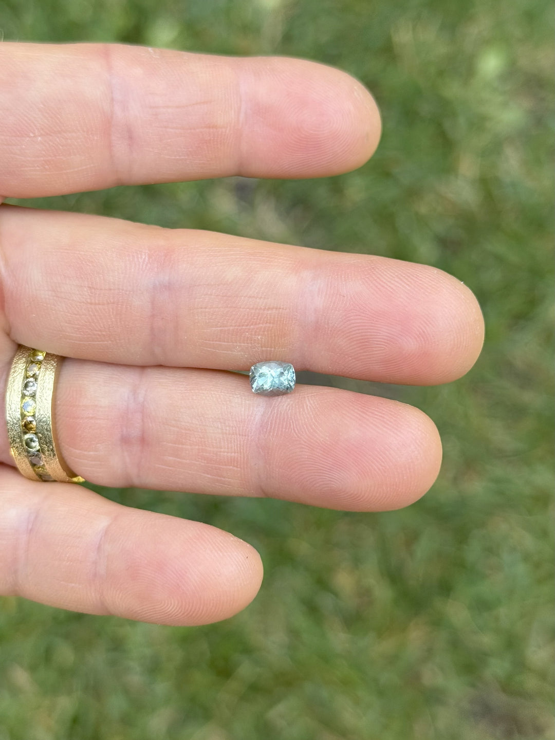 Unheated 1.15ct Montana sapphire shown on fingers for scale, elongated cushion cut with teal and green coloration