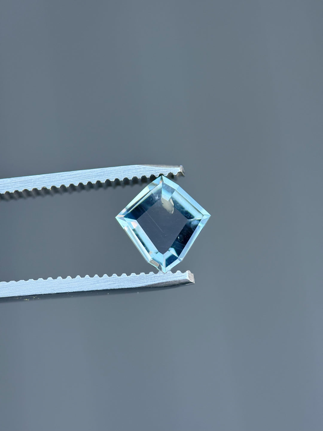 Side view of 1.52ct color change sapphire from Montana, suspended in tweezers to showcase clarity and sharp faceting.