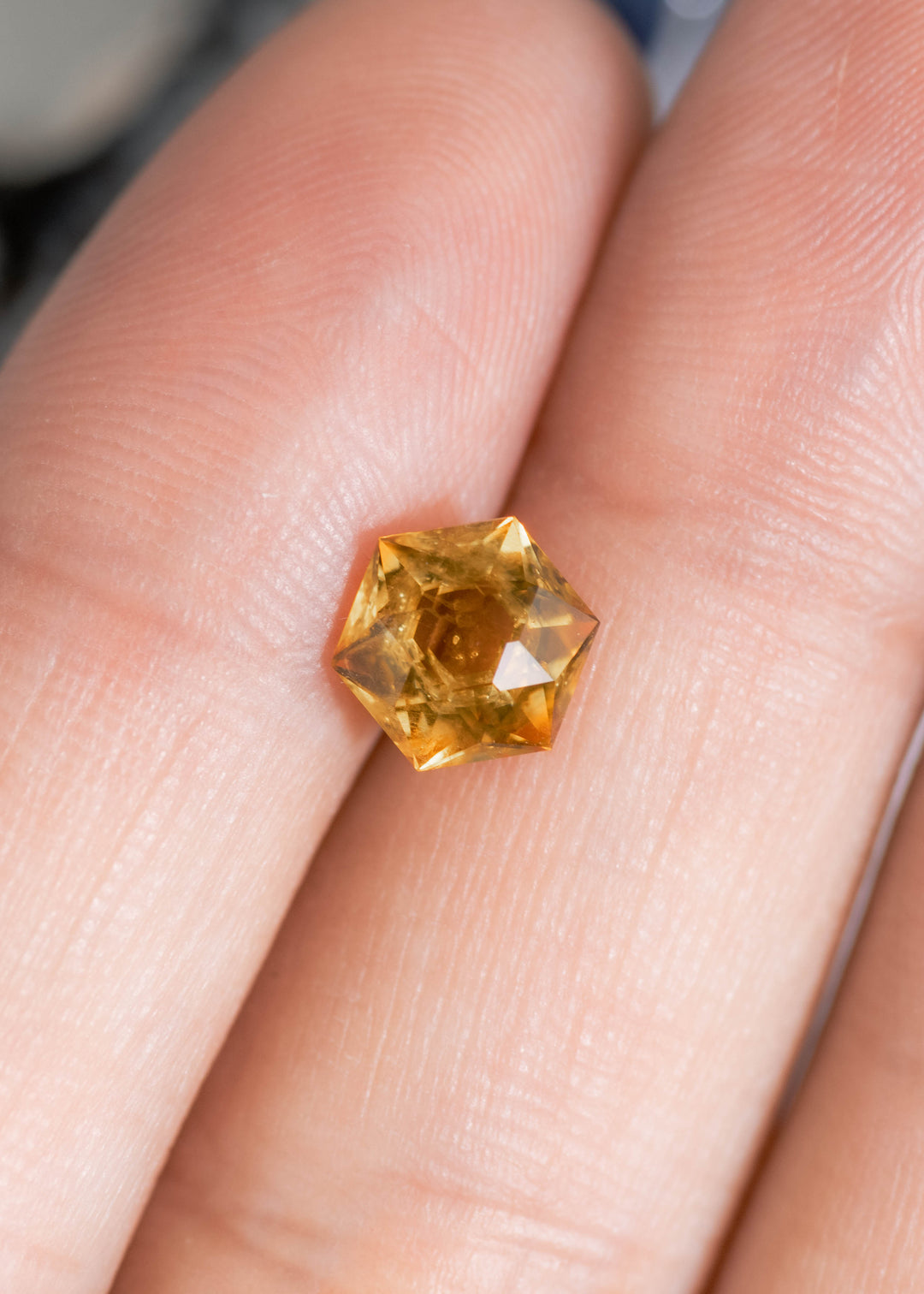 1.88 carat heated orange yellow Montana sapphire hexagonal modified brilliant cut shown on fingers for size reference highlighting rich golden color and sparkle