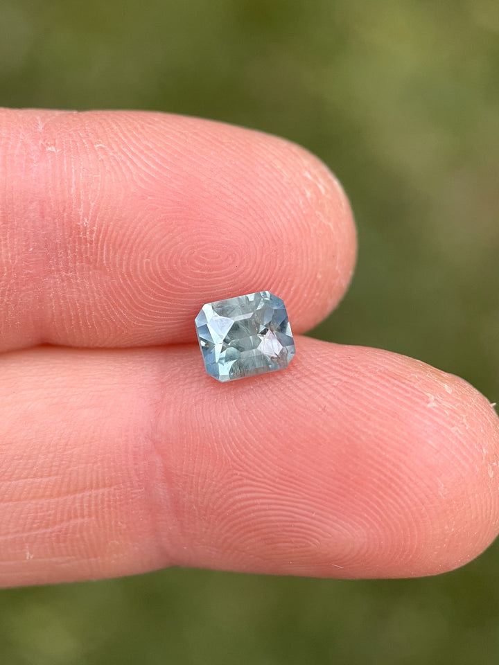 Teal blue-green unheated Montana sapphire held on a fingertip in natural light, displaying a clean octagonal cut and pastel hues.