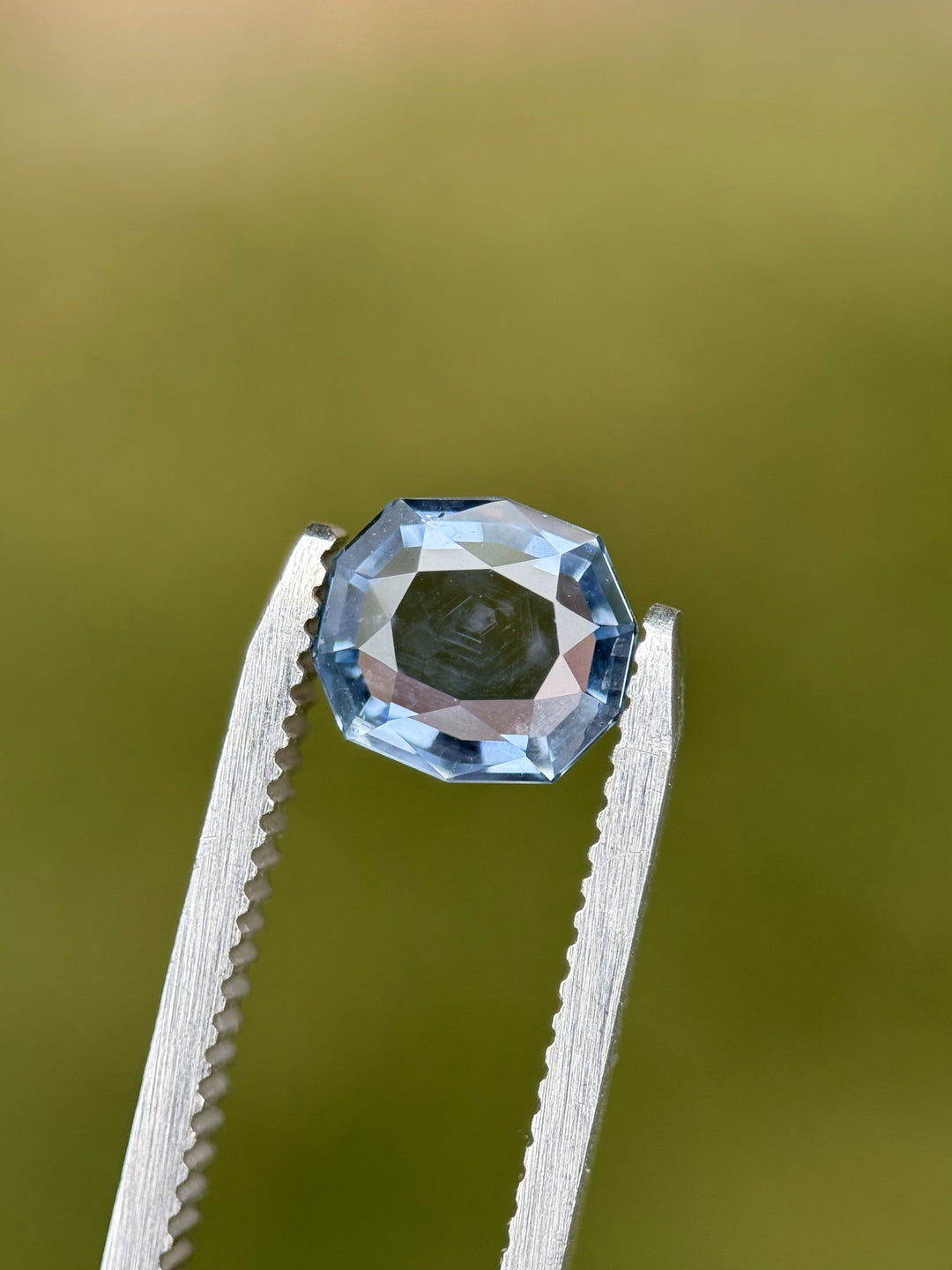 2.08-carat Montana sapphire in custom cushion tablet cut with color-shift blue and violet hues, held in gem tweezers outdoors.