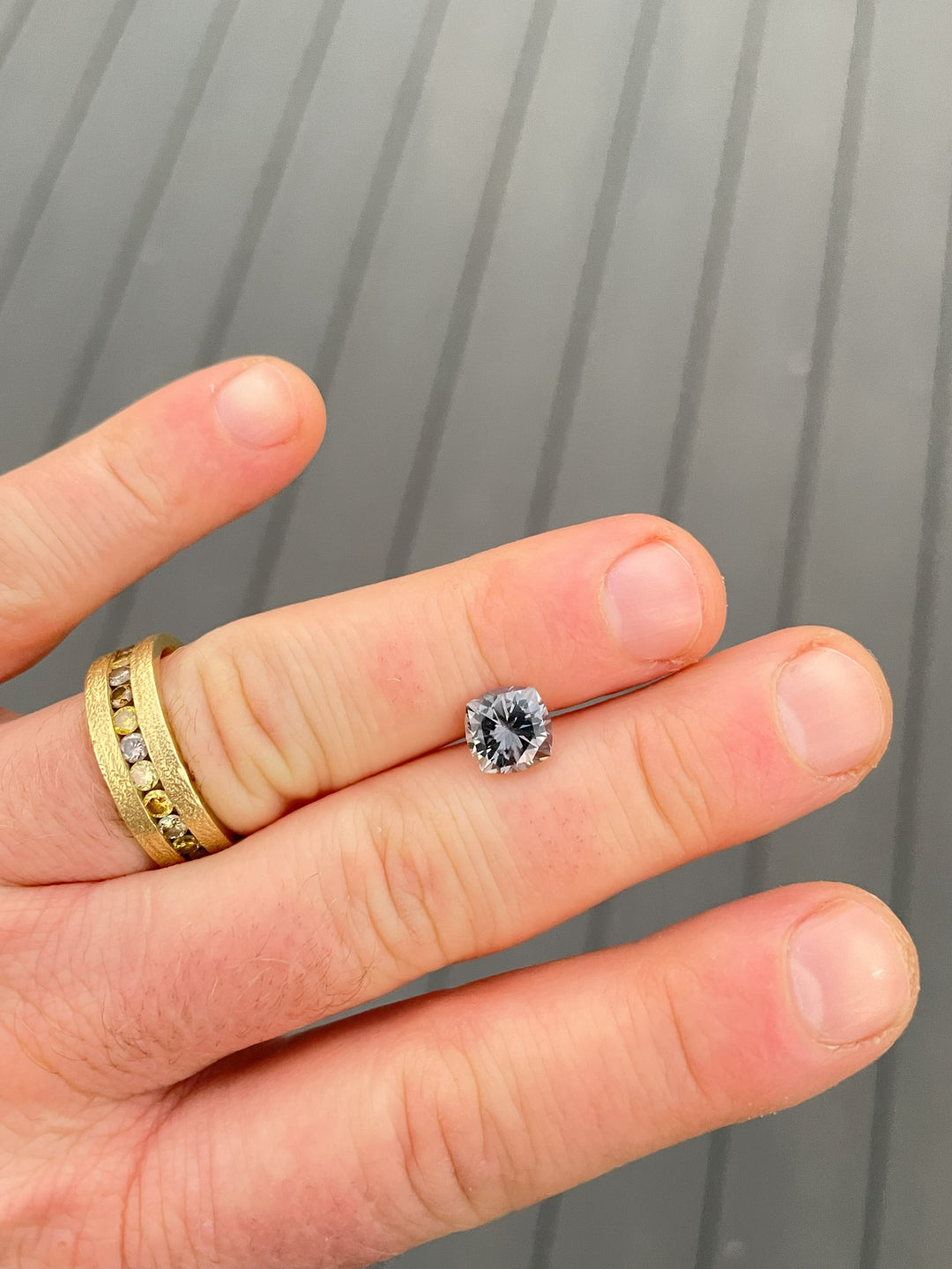 Cushion-cut Montana Sapphire weighing 3.13 carats, displayed on fingertips with its vibrant green and purple hues reflecting natural daylight.
