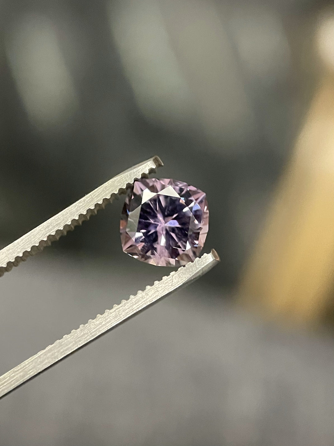3.13 carat Montana Sapphire in a modified cushion cut, held delicately with precision tweezers, showcasing its pinkish-purple color under focused lighting.