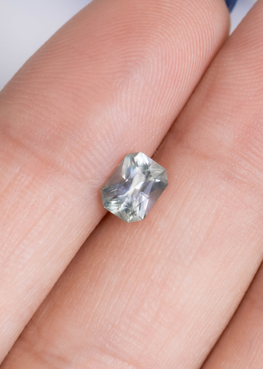 Untreated 0.96ct teal gray blue Montana sapphire mixed radiant cut shown on fingertip for size reference, highlighting precision faceting and natural Montana origin.