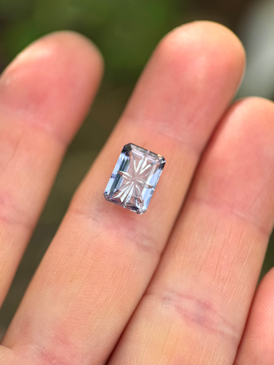 4.01 carat Tanzanite in blue, pink, and purple multi-color tones shown resting on fingers, highlighting the custom concave fantasy emerald cut and internal starburst pattern. Natural Tanzanite from Merelani Hills, Tanzania, untreated.