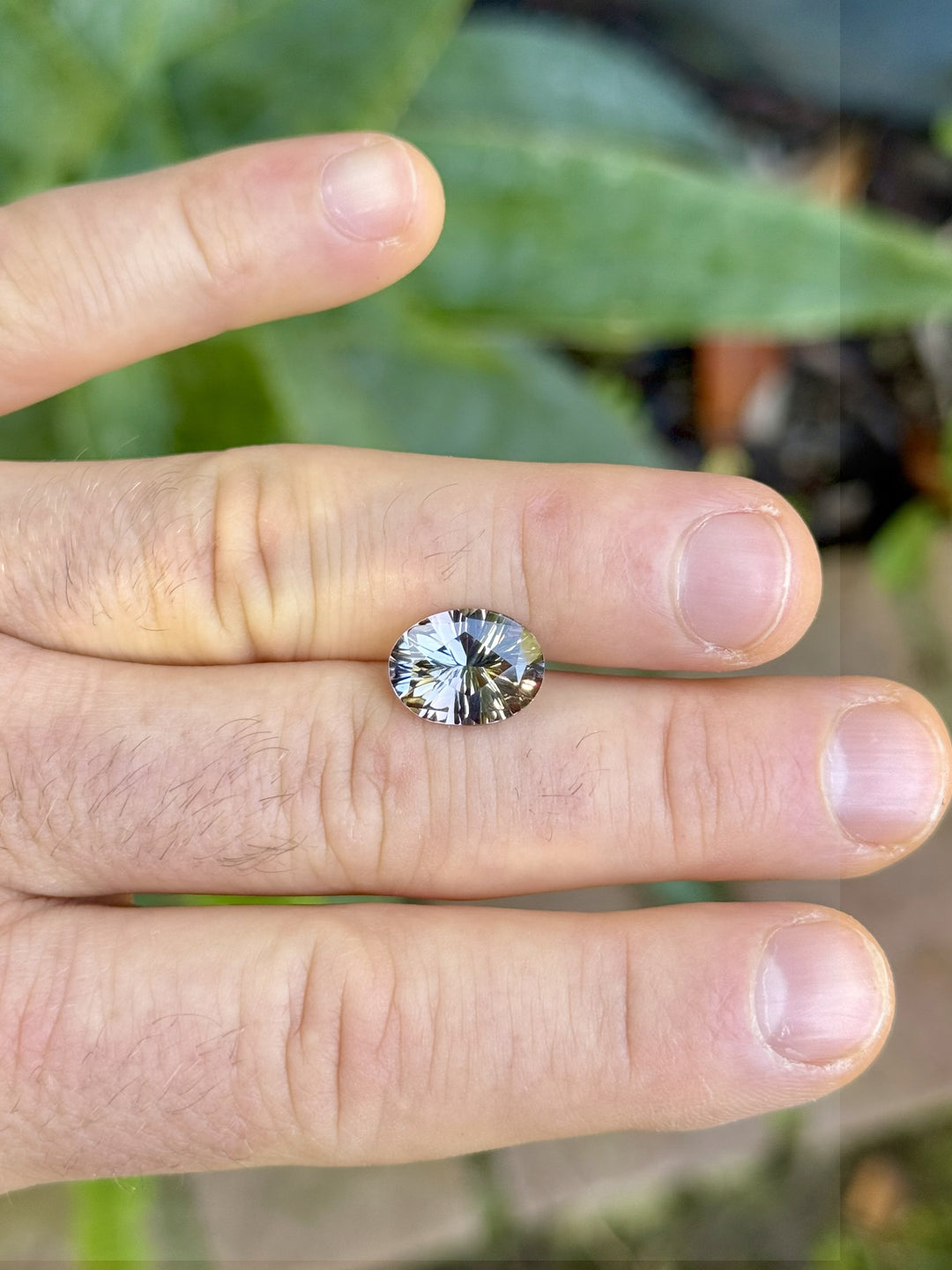Large 4.78ct Tanzanite gemstone displayed on fingers, highlighting the custom oval concave cut and color play of blue, pink, and green under natural light