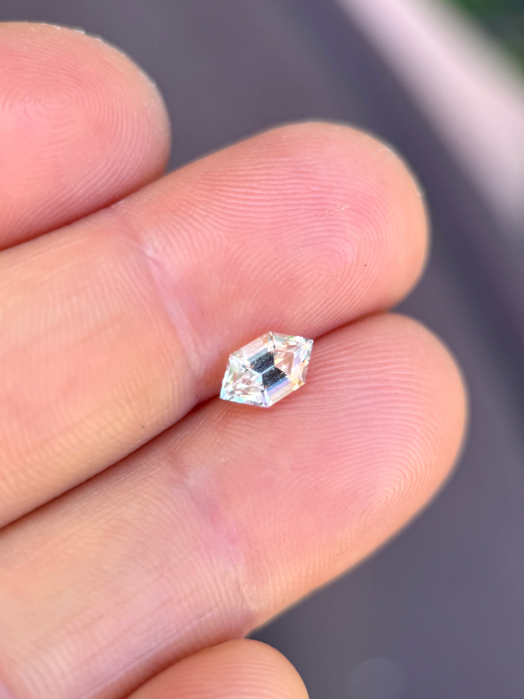 Pale yellow gray sapphire on fingertip showing scale and soft neutral tones, hexagon step cut loose gemstone.