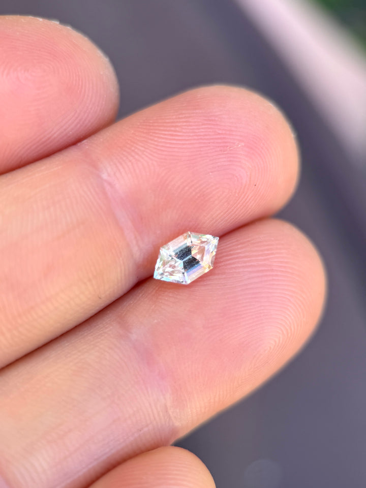 Pale yellow gray sapphire on fingertip showing scale and soft neutral tones, hexagon step cut loose gemstone.