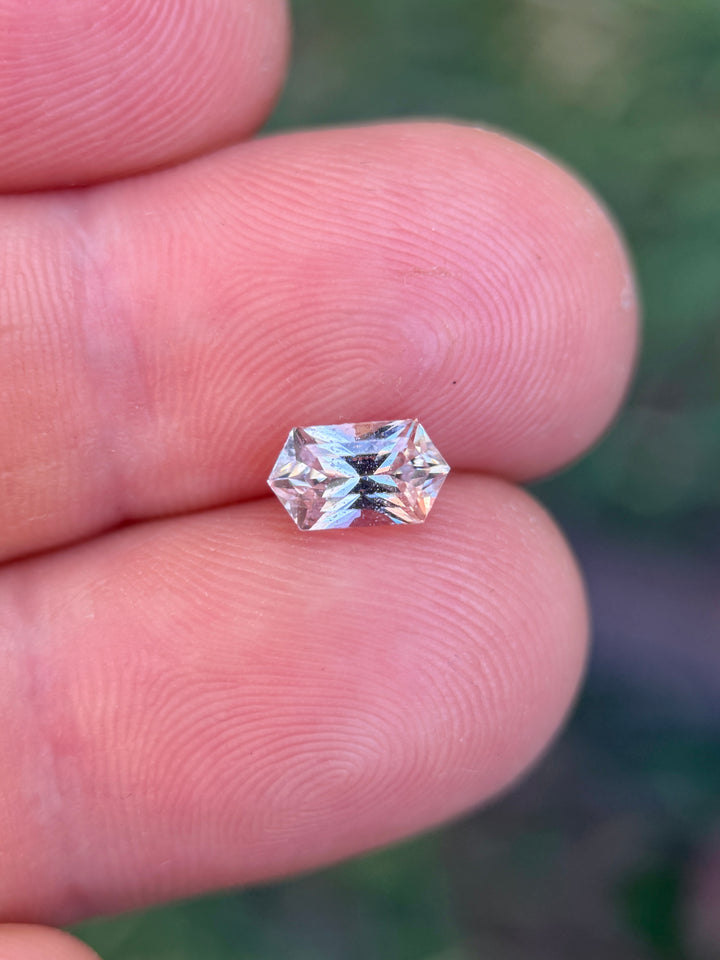 Peach pink hexagon sapphire on finger showing size and soft pastel color, loose gemstone for engagement ring or jewelry.