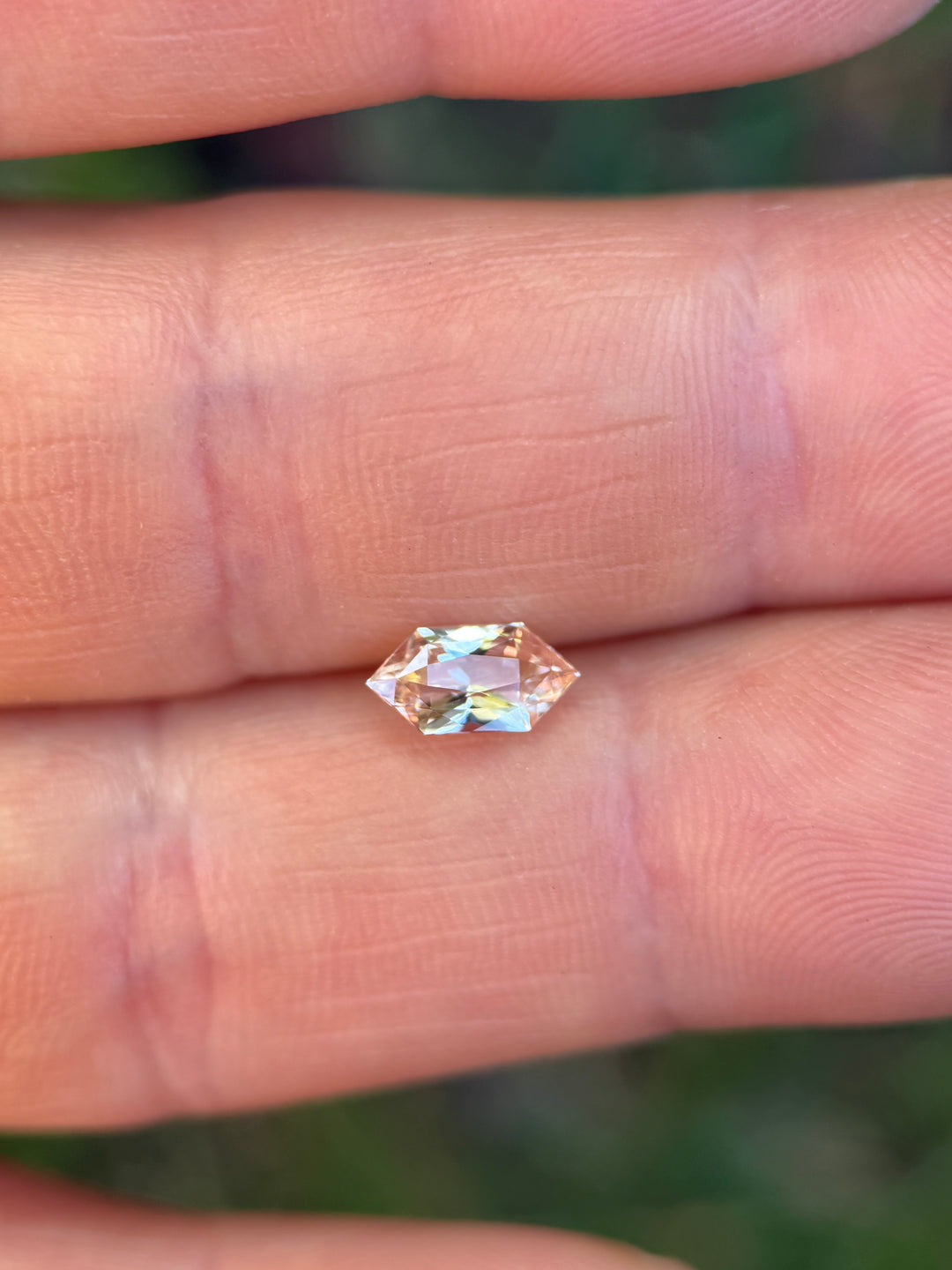 Salmon pink peach sapphire on fingertip showing size and soft color tones, elongated hexagon loose gemstone.